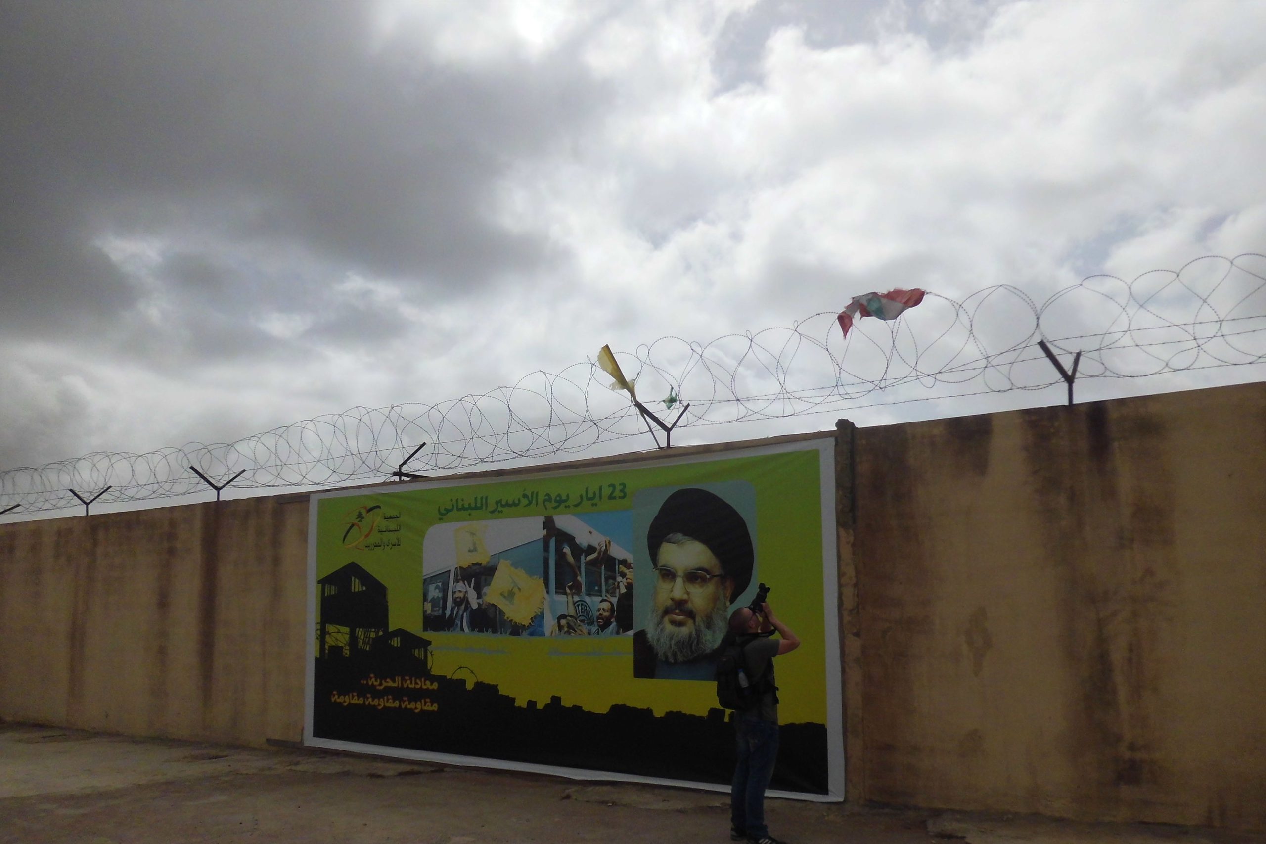 2. Frente a un cartel de la Hezbolá con una imagen de su líder, el jeque Hasan Nasralah, un fotógrafo intenta captar los jirones de una bandera libanesa enganchada al alambre de espino que delimita el centro de Khiam. En el ángulo inferior izquierdo se puede leer: “Fórmula de la libertad: resistencia, resistencia, resistencia”. Sobre todo el recuerdo de la encarcelación y las torturas infringidas a los miembros de Hezbolá ocupan una parte importante de la tarea del centro. Varios guías, todos ex prisioneros del campo por días, meses e incluso años, explican al visitante cómo funcionaba la cárcel mientras enseñan el interior de sus restos.