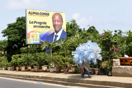 Un hombre carga botellas de plástico junto a un anuncio de campaña del actual presidente de Guinea Conakry, Alpha Conde. Seyllou Diallo/AFP/Getty Images