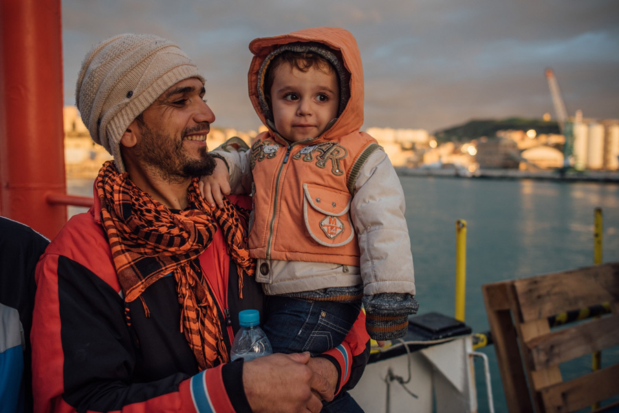 Un hombre y su hijo encuentran tiempo para posar en una fotografía poco antes de atracar en Italia, después de una horrorosa travesía y rescate por la noche en medio del mar Mediterráneo, en unas condiciones espantosas. Imagen de Kevin McElvaney.