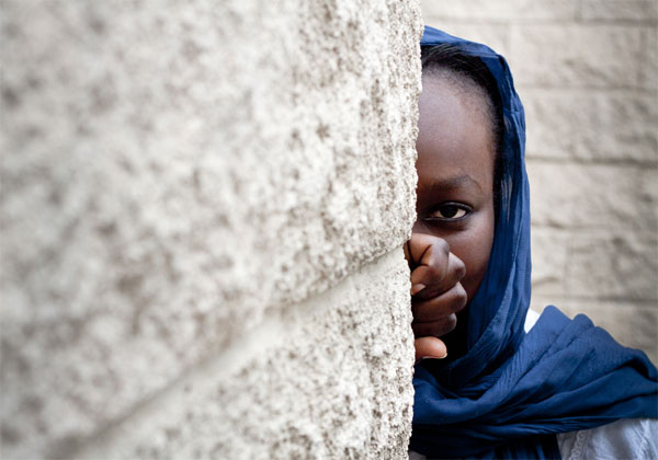 La quema sistemática de casas y aldeas enteras, los asesinatos masivos y la limpieza étnica y religiosa han obligado a desplazarse a miles de personas. Nacida en el exilio, posiblemente, nunca conocerá la tierra de sus padres: Sudán. Refugiada reasentada en España, 2012. Esta joven de origen sudanés fue reasentada en España junto a su familia en 2012. Huyeron de la guerra en Libia y encontraron refugio en el campo de Shousha, en Túnez, donde vivieron más de un año. Su padre, profesor de profesión en su Sudán natal, trata ahora de rehacer su vida en España y de aprender el idioma para, según información proporcionada por ACNUR: conocer mejor a la gente española. Para sus cinco hijas, el proceso de integración está siendo algo más fácil, aunque no está exento de dificultades, sobre todo por los problemas económicos a los que deben hacer frente. Sudán es un país que lleva décadas inmerso en un conflicto con Sudán del Sur. Según datos de la Agencia de Refugiados, la quema sistemática de casas y aldeas enteras, los asesinatos masivos y la limpieza étnica y religiosa han obligado a desplazarse a miles de personas que nacidas en el exilio, probablemente, nunca conozcan la tierra de sus progenitores. El 44% de la población del país vive con menos de 2 dólares al día y el 46,5% de la población vive bajo el umbral de la pobreza, con un marcado contraste entre las zonas urbanas y rurales. Asimismo, apenas el 64% de la población está alfabetizada. Por lo tanto, Sudán continúa siendo uno de los países menos desarrollados del mundo. ©ACNUR/UNHCR/F.Magallón
