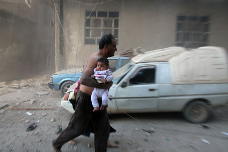 Un hombre sirio carga con un bebe huyendo de los bombardeos. Amer Almohibany/AFP/Getty Images