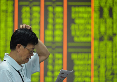 Un inversor lee el periódico junto a una pantalla que muestra los precios de las acciones de una empresa de seguridad en Hangzhou, al este de la provincia de Zhejiang en China. (STR/AFP/Getty Images)