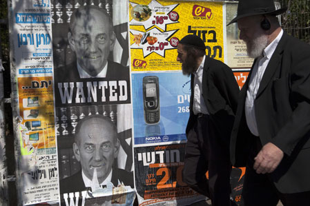 Dos hombres pasan al lado de un poster con la imagen del ex primer ministro israelí Ehud Olmert y la frase "se busca", en relación a los casos de corrupción en los que se ha visto envuelto el ex dirigente. AFP/Getty Images