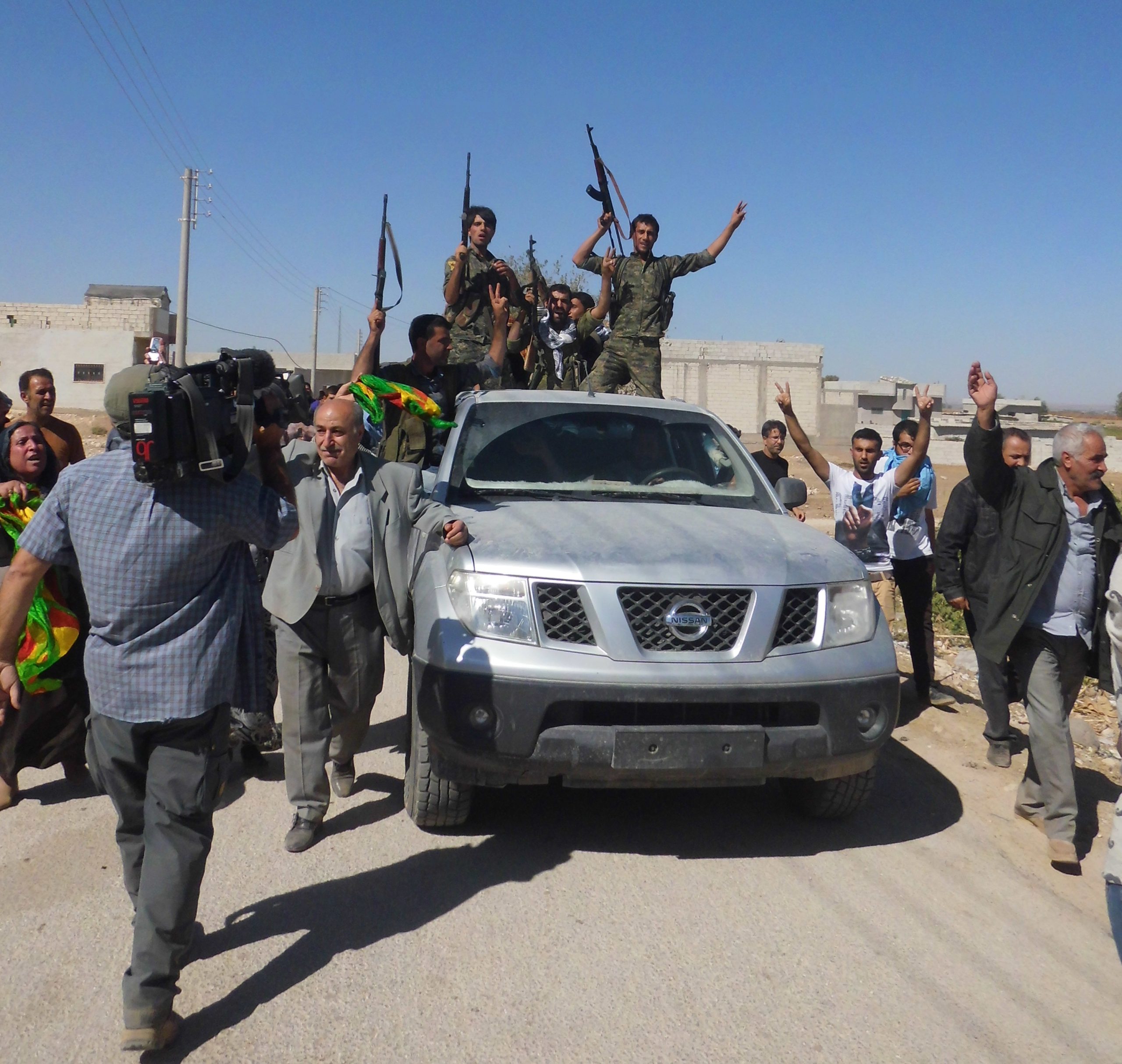 En el corazón de la ciudad. El viernes 26 de septiembre unas mil personas, pertenecientes a movimientos prokurdos, socialistas, comunistas e incluso kemalistas, habían conseguido llegar desde Turquía al enclave kurdo en el norte de Siria después de tumbar por la fuerza el tendido del alambre de espino de la frontera. Deseaban mostrar su solidaridad con los sitiados, algo que despertó unas pocas horas de alegría. En la foto, miembros de las milicias kurdas de la Unidad de Protección del Pueblo (YPG) hacen la señal de la victoria y disparan al aire como gesto de celebración en el centro de Kobane. Ese 26 de septiembre fue un día inusual allí: la ciudad sitiada pudo darse un respiro del acoso al que le tiene sometido el Estado Islámico desde hace semanas. Foto y texto: Ricardo Ginés